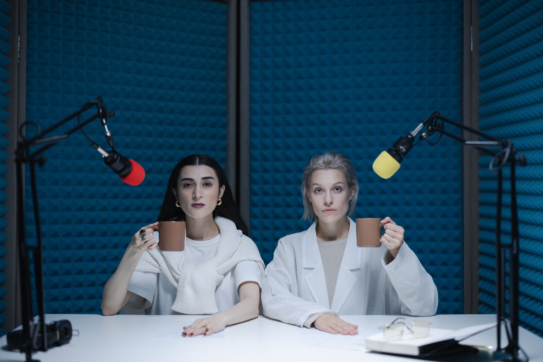 Two creators in a soundproof podcast studio with microphones